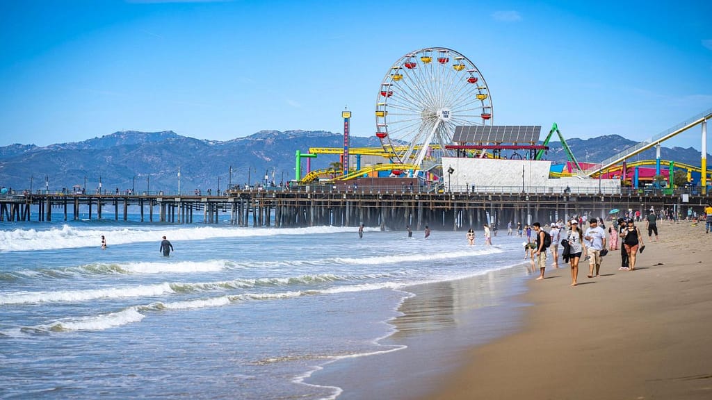 People walking and swimming near Santa Monica Pier with the ferris wheel on a sunny day
