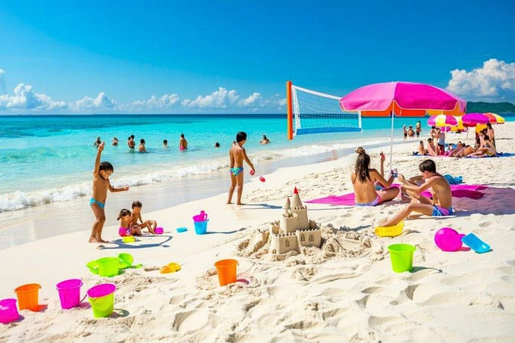 cancun-family-relaxing-beach-umbrella-1200x800 | Go With The Family Family relaxing on beach with kids playing in Cancun