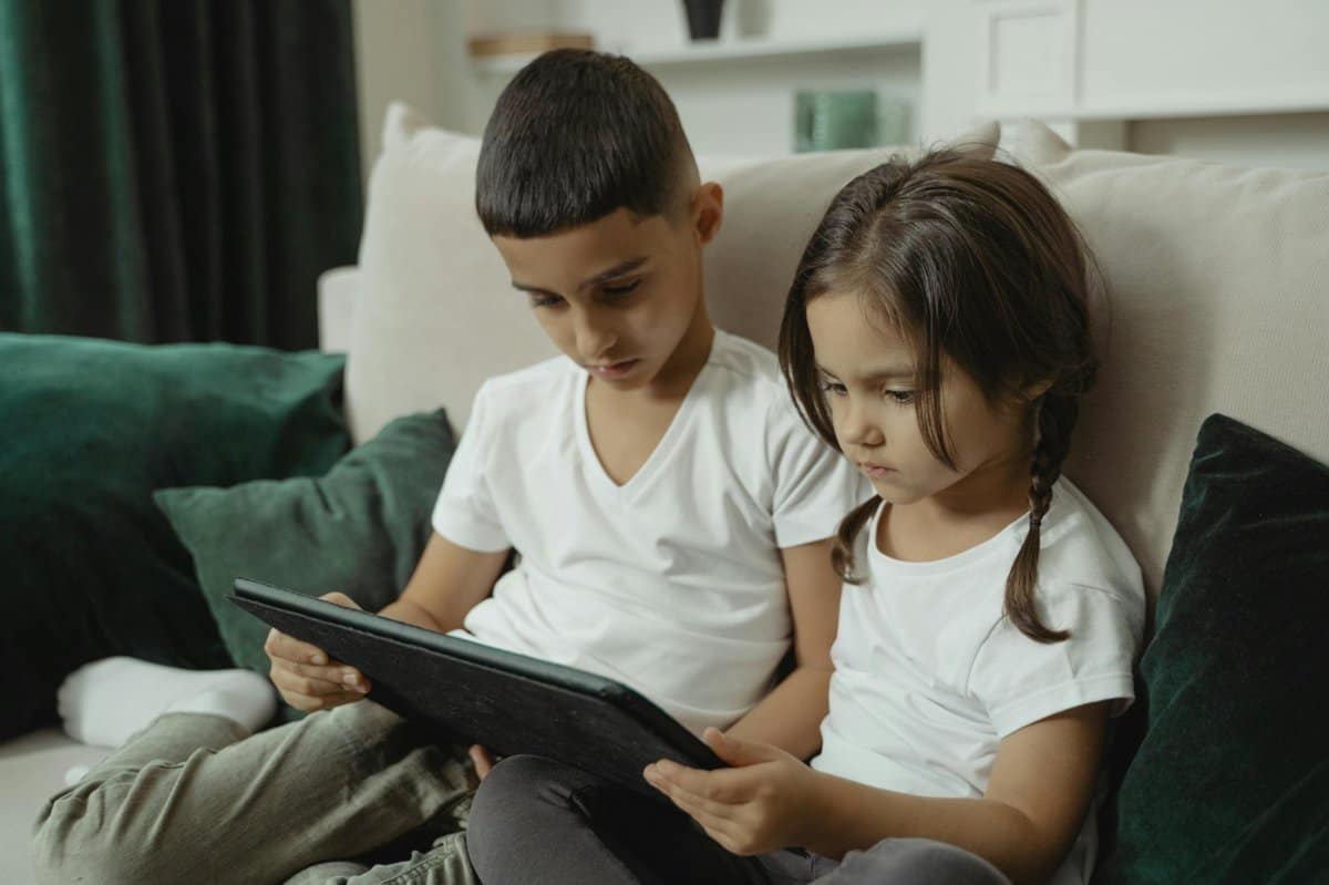 a6b6945b-78ff-4ae9-9d31-30531c5ad718_1200 | Go With The Family Two kids sitting on a couch using a tablet while relaxing during a family trip