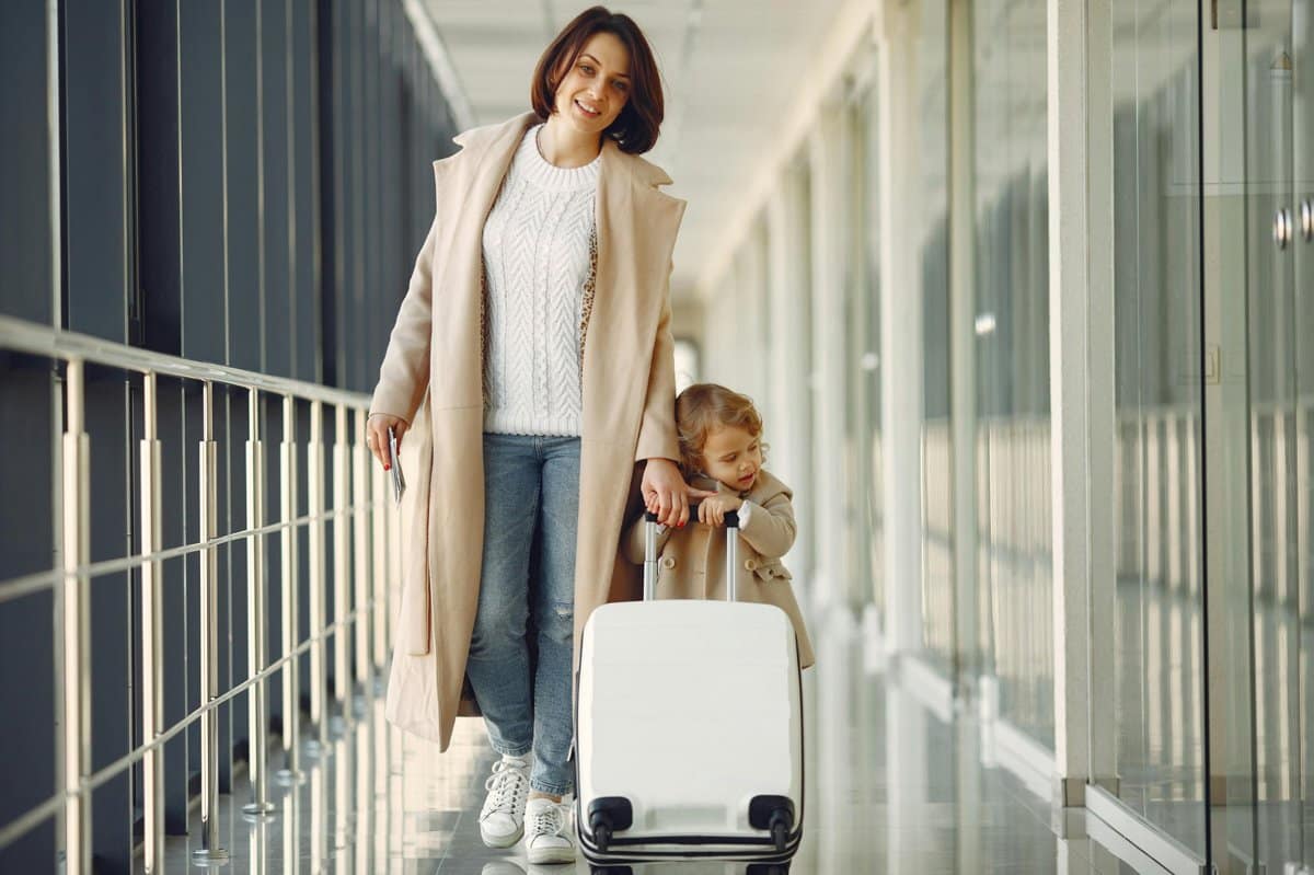b26abfee-a855-44bc-9a24-712b700e8e4b_1200 | Go With The Family Mother and child walking through an airport with luggage during a family trip