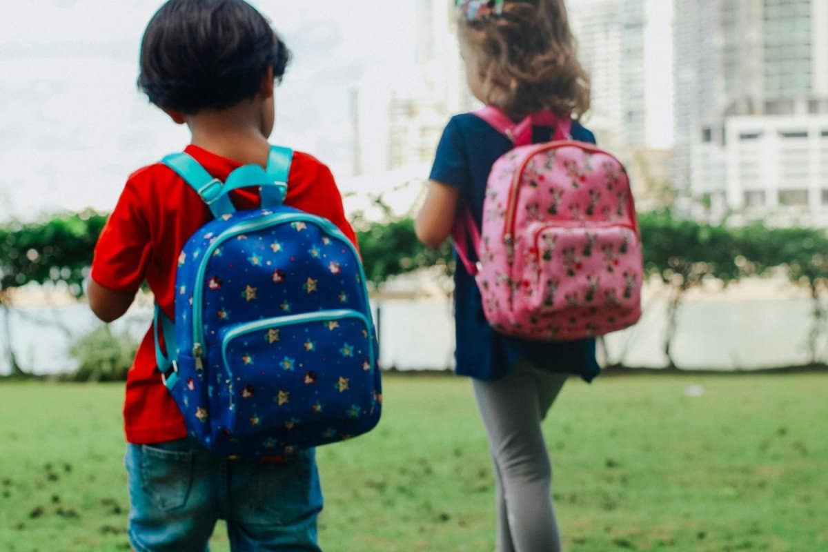 family-with-backpacks-at-airport-gate_1200x800 | Go With The Family Two young children wearing colorful backpacks walking together outdoors, symbolizing kid-friendly carry-on bags.