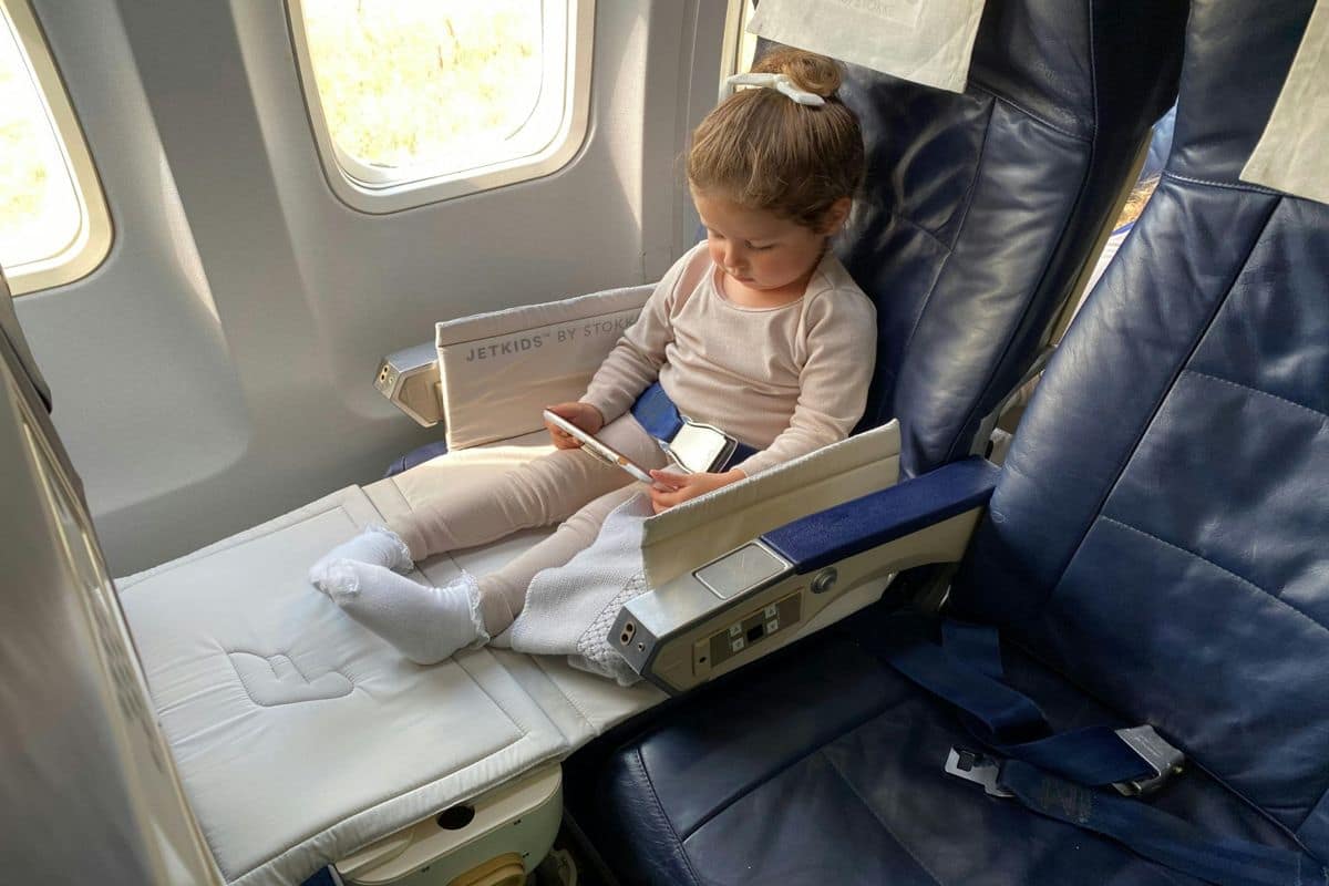 girl-on-airplane-footrest | Go With The Family Young child using a footrest and watching a tablet on an airplane