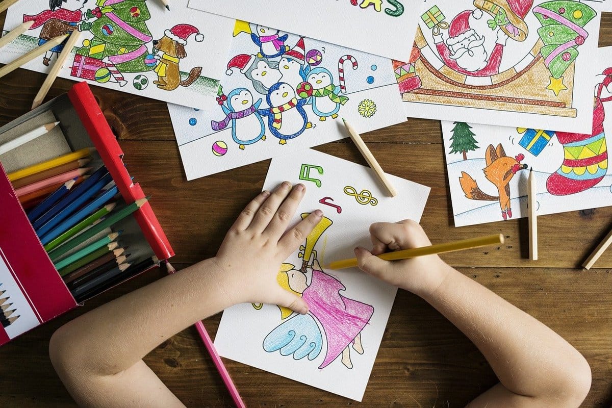 kids-travel-activity-kit_1200x800 | Go With The Family Child coloring Christmas-themed activity pages at a table, representing a travel activity kit for kids