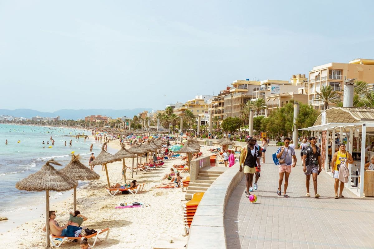 Family Beach Holidays in Ibiza, Spain | Go With The Family Busy beach and seaside promenade in Ibiza, Spain, with visitors enjoying the Mediterranean coastline.