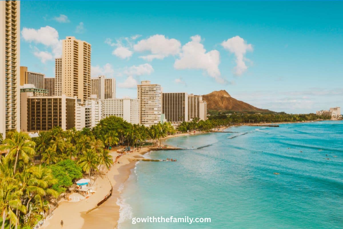 Waikiki Beach, Oahu, Hawaii | Go With The Family Waikiki Beach in Oahu, Hawaii, with palm trees, beachfront hotels, turquoise water, and Diamond Head crater in the background.