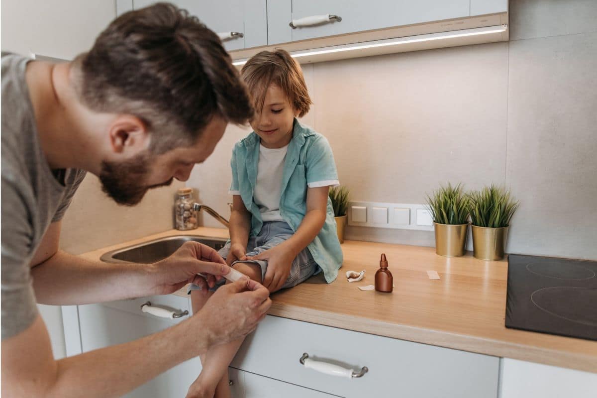 Family Travel Health & Wellness Essentials | Go With The Family Parent applying a bandage to a child's knee as part of family travel health and wellness essentials.