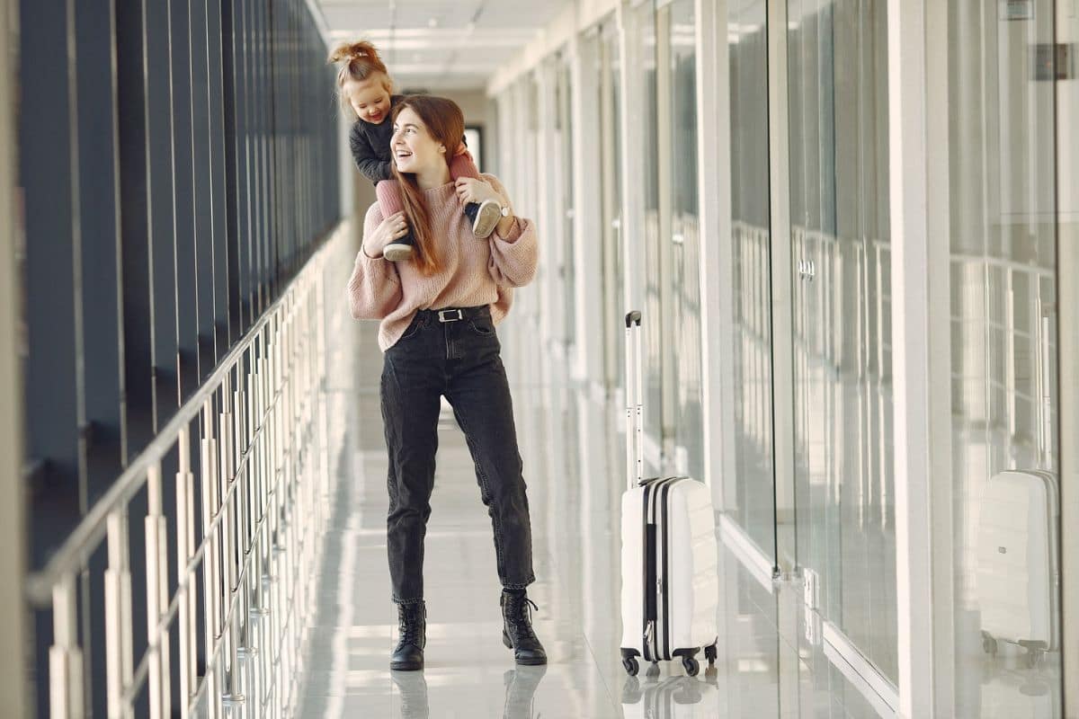 Mother Carrying Toddler at Airport | Go With The Family Mother carrying her toddler through an airport terminal during a family trip.
