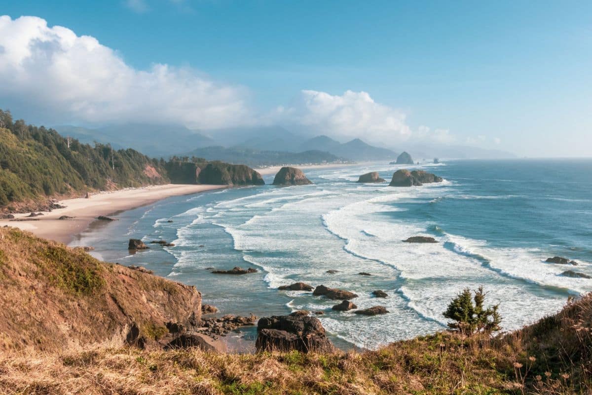Pacific Northwest Oregon Coast Family Road Trip | Go With The Family Rugged Oregon coast with sea stacks and forested mountains on a Pacific Northwest family road trip