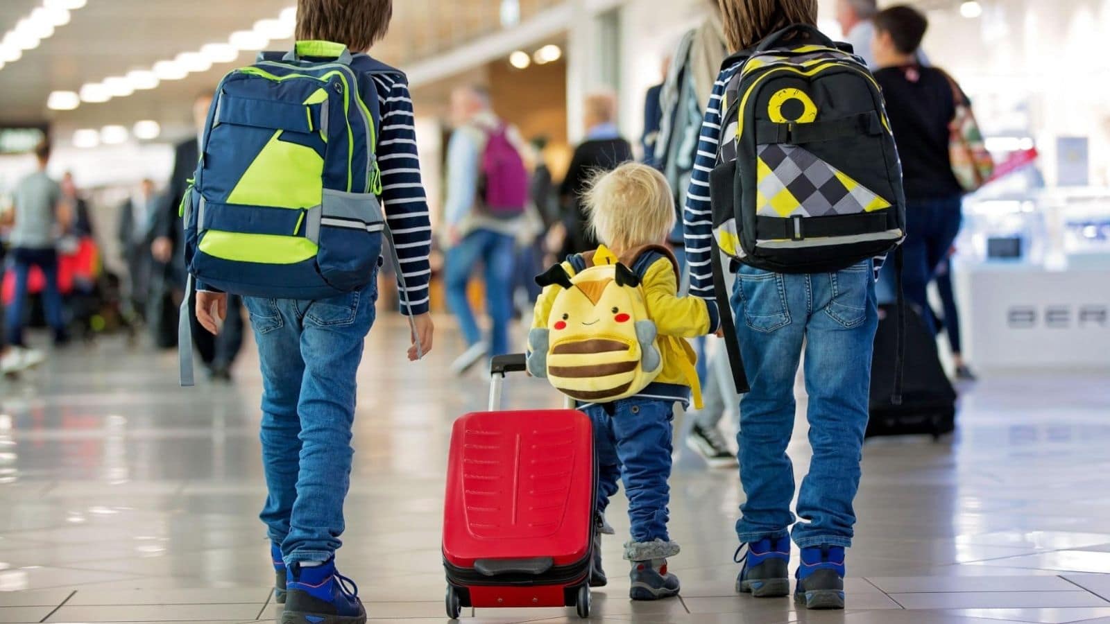 family-travel-gear-essentials-airport-hero-1600x900 | Go With The Family Family walking through an airport with luggage and travel gear before a vacation.
